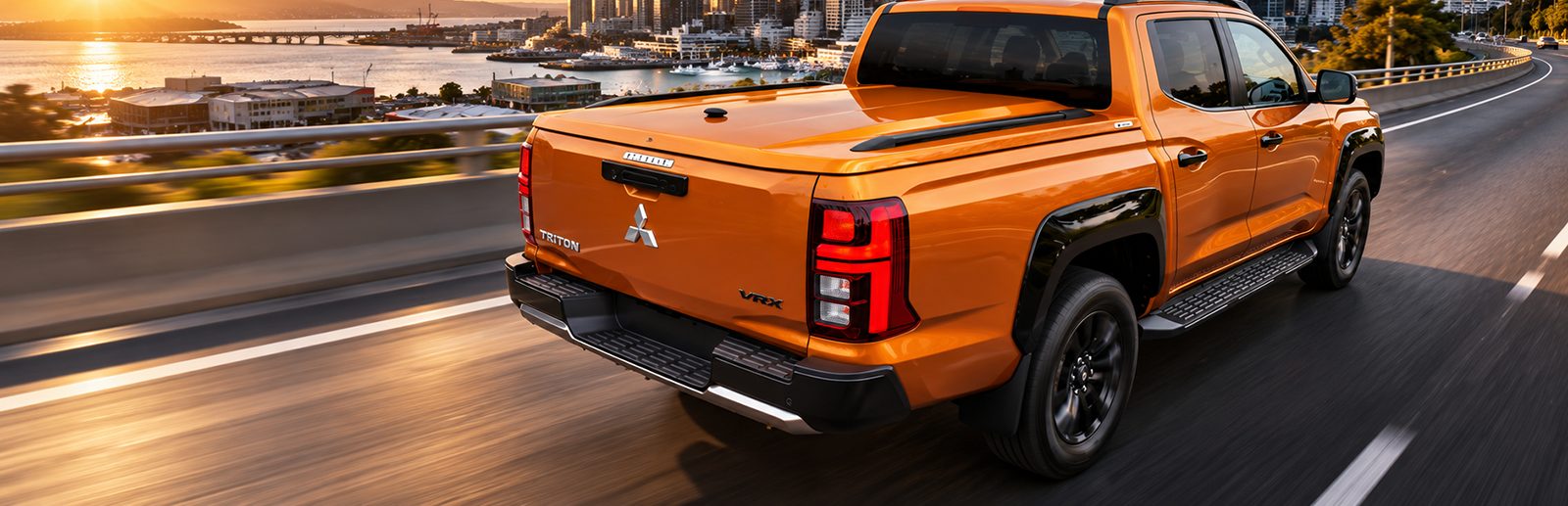 Orange Mitsubishi Triton with a colour-matched Sport Lid SV driving on a city motorway at sunset